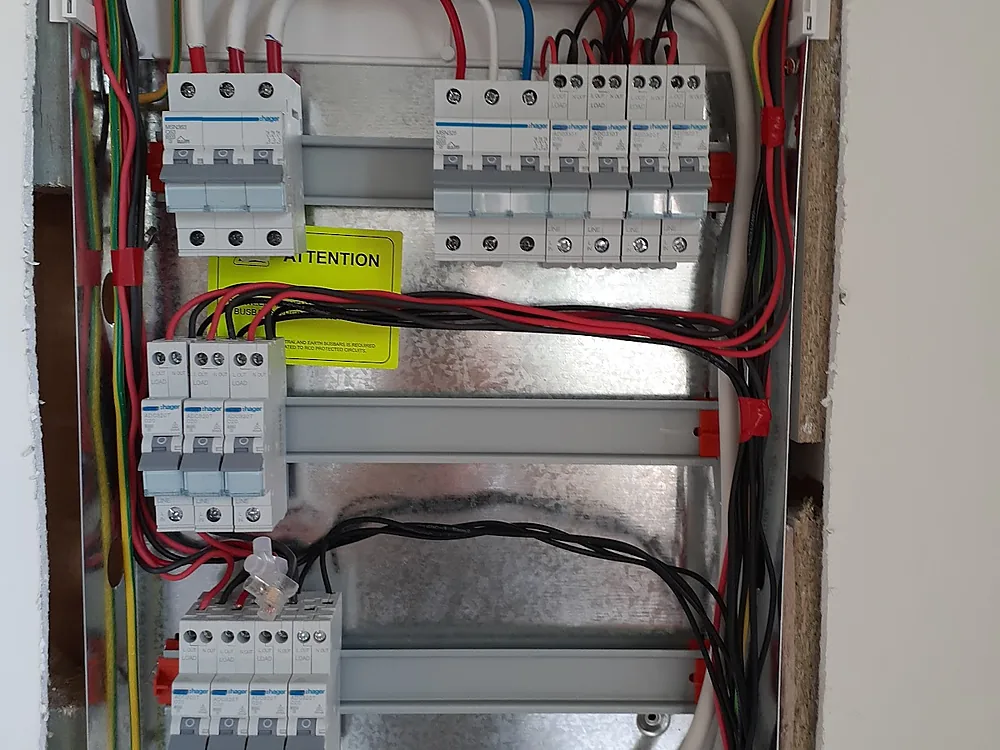 New switchboard with rows of circuit breakers and safety switches, neatly wired in a white enclosure
